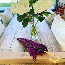 Load image into Gallery viewer, A closed japarra umbrella with japarra box on a table. The world's most beautiful way to protect your skin.Block damaging UV sun rays and the rain with this stunning umbrella, also called parsol, in pink and purple 100% cotton. Save your skin and protect your investment in skincare by stopping the sun's damaging UV rays, carry this lightweight japarra umbrella everywhere. This is a beautiful sun umbrella, also called a parasol, in 100% cotton colorful prints.
